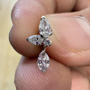 May include: A silver-toned earring featuring a cluster of three clear, faceted stones arranged in a butterfly-like shape, with one pear-shaped stone, one marquise-shaped stone, and one round stone, plus a dangling marquise-shaped stone below.