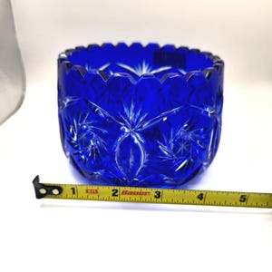 Op de afbeelding: Een helderblauwe, geslepen glazen kom met een sterrenpatroon. De kom heeft een diameter van ongeveer 10 cm, met een geschulpte rand. De kom is gemaakt van dik, helder glas.