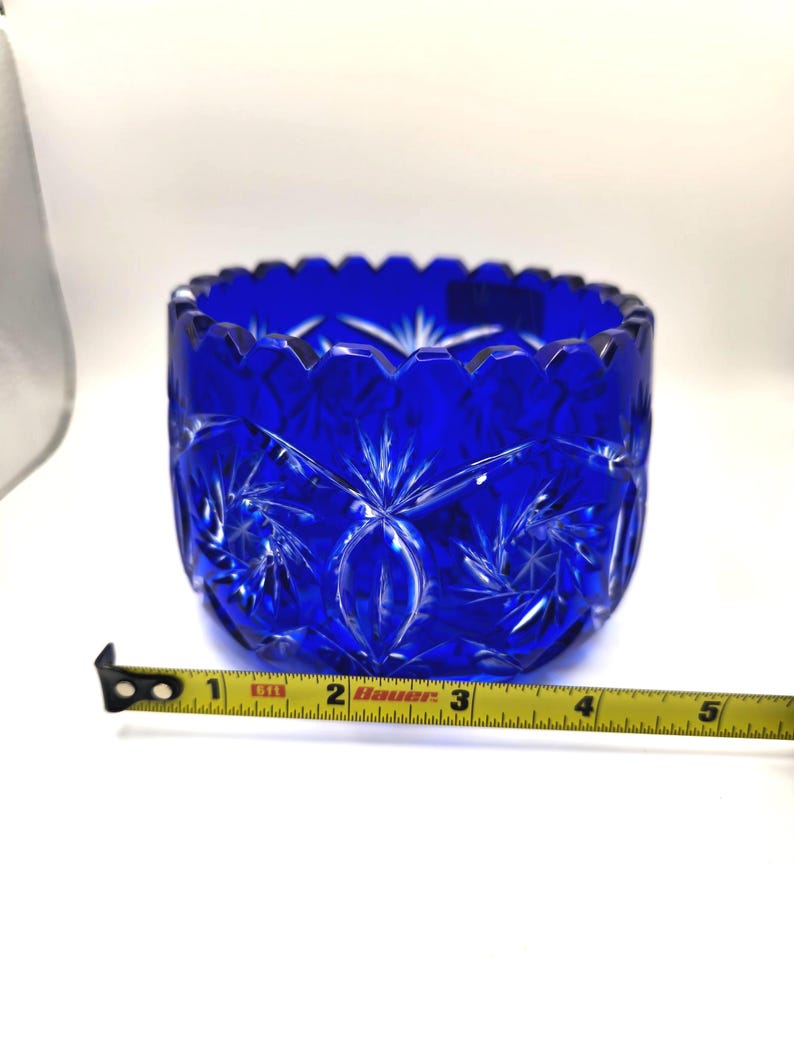 Op de afbeelding: Een helderblauwe, geslepen glazen kom met een sterrenpatroon. De kom heeft een diameter van ongeveer 10 cm, met een geschulpte rand. De kom is gemaakt van dik, helder glas.