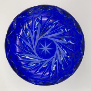 Op de afbeelding: Een diepblauwe, ronde glazen kom met ingewikkelde stervormige en geometrische patronen. Het ontwerp van de kom heeft een centraal stermotief omgeven door stralende lijnen en gedetailleerde sneden, waardoor een textuur ontstaat.