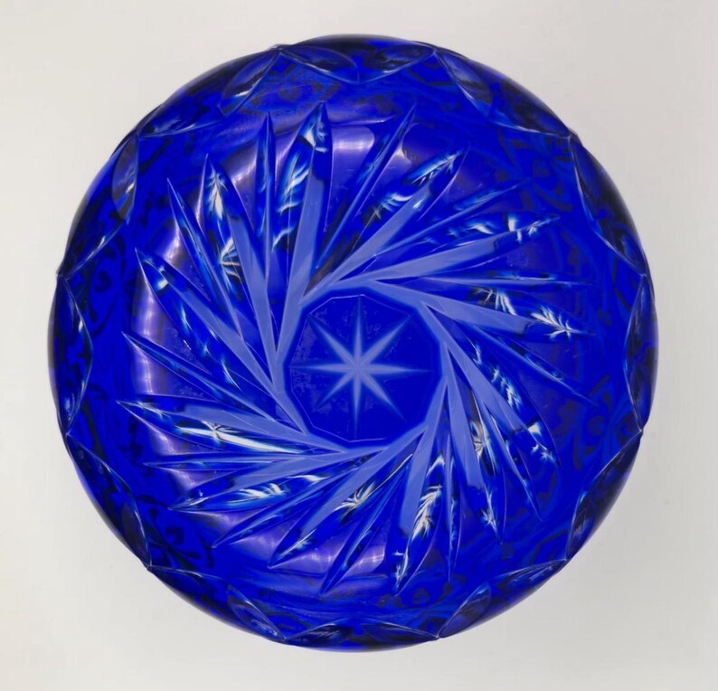 Op de afbeelding: Een diepblauwe, ronde glazen kom met ingewikkelde stervormige en geometrische patronen. Het ontwerp van de kom heeft een centraal stermotief omgeven door stralende lijnen en gedetailleerde sneden, waardoor een textuur ontstaat.