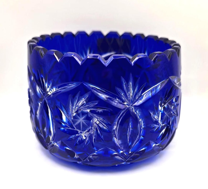 Op de afbeelding: Een diepblauwe, geslepen glazen kom met een geschulpte rand. De kom heeft ingewikkelde patronen van sterren en bloemen, waardoor een sprankelend effect ontstaat. Deze decoratieve kom is ideaal om te serveren of tentoon te stellen.