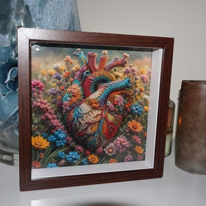 May include: A square dark brown wooden frame containing a colorful print of an anatomical heart intricately woven with vibrant floral patterns. The heart is surrounded by a dense field of multi-colored wildflowers in shades of orange, blue, and pink.