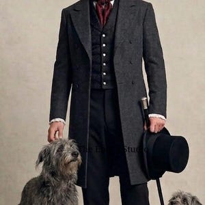 Könnte beinhalten: Ein anthrazitfarbener Wollmantel über einer schwarzen gemusterten Weste mit silbernen Knöpfen, einem weißen Hemd mit Kragen und einem dunkelroten Plastron. Das Outfit umfasst eine schwarze Hose, einen schwarzen Zylinder und einen schwarzen Gehstock.