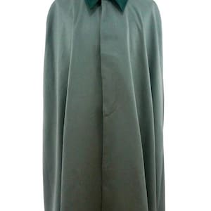 Puede incluir: Una capa verde salvia con cuello verde oscuro exhibida en un maniquí. La capa tiene un diseño sencillo y un cierre de botón en el cuello. La tela parece ser de peso medio.