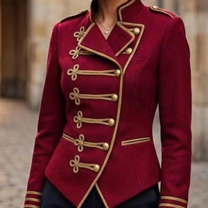 May include: A deep burgundy military-style jacket featuring a high collar, gold-toned piping, and a double-breasted front closure with five round gold buttons and decorative braided cord loops. The sleeves have three horizontal gold stripes at the cuffs.