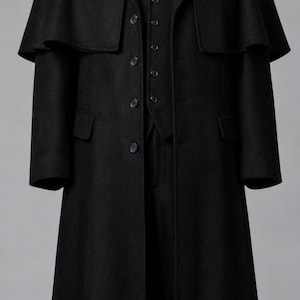May include: A black wool-blend overcoat featuring a shoulder cape, long sleeves, and a button-front closure. Underneath, a black vest with a button-front is worn over a crisp white collared shirt with a black necktie, displayed on a mannequin.