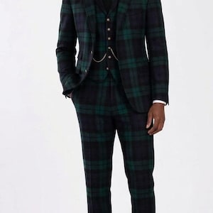 May include: A three-piece suit in a green and navy plaid pattern. The suit includes a jacket, vest, and trousers. The jacket has a black velvet collar. The vest has a gold chain. The suit is worn with a white dress shirt and black tie.