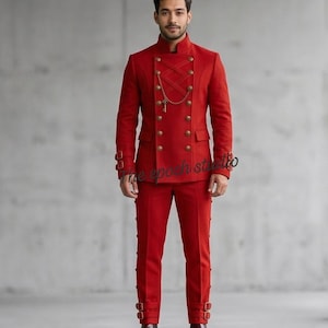 May include: A red suit with a high collar and double-breasted design. The jacket features gold-colored buttons and a decorative chain. The pants have buckle details at the ankles. The suit is a bold, formal outfit.