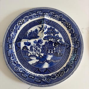 Puede incluir: Plato de servir dividido azul y blanco con un clásico patrón Willow. El plato presenta una escena central de paisaje con un puente, árboles y edificios, rodeada por un borde decorativo. El plato está dividido en tres secciones.