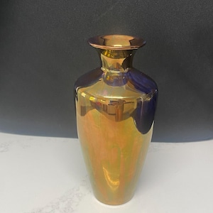 May include: A decorative vase with a metallic finish. The vase has a slender neck and a rounded body. The colors include gold, bronze, and hints of blue and green. The vase is approximately 8 inches tall.