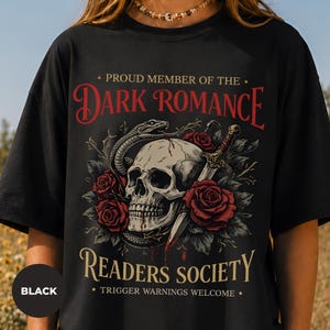 Puede incluir: Una camiseta negra con un estampado gráfico de un cráneo humano entrelazado con una serpiente y una daga, rodeado de rosas rojas. El texto dice: PROUD MEMBER OF THE DARK ROMANCE READERS SOCIETY. TRIGGER WARNINGS WELCOME.