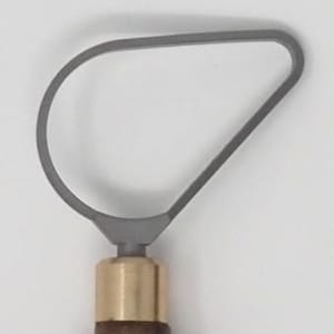 May include: A gray loop tool for pottery or sculpting, featuring a curved metal loop attached to a wooden handle with a brass ferrule. The tool is designed for shaping and removing clay.