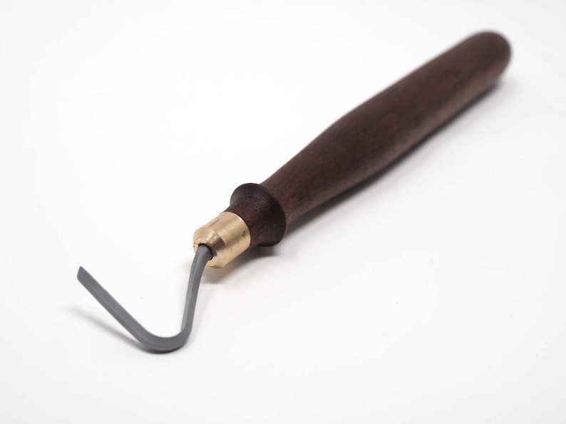 May include: A pottery tool with a dark brown wooden handle, a brass ferrule, and a gray, curved metal loop. The tool is designed for shaping and detailing clay. The handle is smooth and ergonomic.