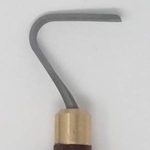 May include: A close-up of a gray, curved metal blade with a brass ferrule and a dark brown wooden handle. The blade is approximately 1 inch wide and has a rounded tip. The tool is likely used for sculpting or carving.