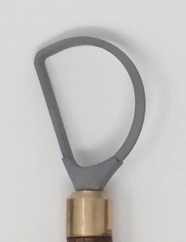 May include: A gray loop tool for pottery or sculpting. The loop is attached to a brass ferrule and a wooden handle. The tool is designed for shaping and removing clay.