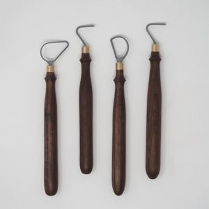 May include: Four pottery tools with dark brown wooden handles and brass-colored ferrules. The metal ends are gray and have different shapes, including a loop and a hook. The tools are arranged against a white background.