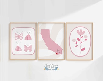 Può includere: Tre stampe artistiche incorniciate con una combinazione di colori rosa chiaro e beige. Le stampe presentano illustrazioni di farfalle, un contorno rosa della California con il testo "San Diego" e un motivo floreale. Le cornici sono di colore legno chiaro.