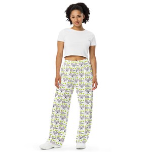 May include: White wide-leg pants with a repeating pattern of tennis rackets and tennis balls. The rackets are purple and the balls are green. The person is wearing a white crop top.