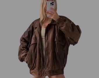 May include: A brown leather jacket with a relaxed fit. The jacket features a collared neckline, two front pockets, and a button-up closure. The jacket has a vintage aesthetic.