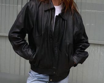 Puede incluir: Chaqueta de cuero negra con cuello, cierre de botones y dos bolsillos delanteros. La chaqueta tiene un dobladillo y puños acanalados. La modelo lleva una camiseta blanca y vaqueros azules.