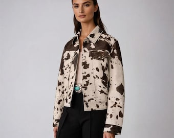May include: A cowhide-patterned jacket in cream and brown. The jacket has a classic collar, button-up front, and two chest pockets. The jacket is paired with black pants and a turquoise belt buckle.