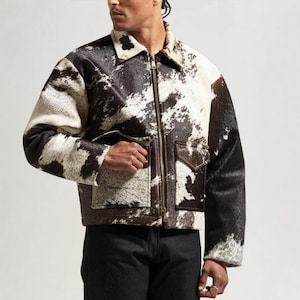 Op de afbeelding: Korte jas met een koeienhuidpatroon in zwart, wit en bruin. De jas heeft een kraag, een ritssluiting en twee voorzakken. Een opvallend kledingstuk.