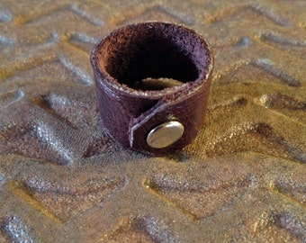 May include: A brown leather ring with a silver metal snap closure.