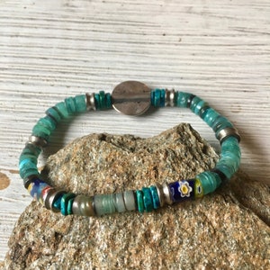 May include: A turquoise and silver bracelet with a round silver charm. The bracelet is made of various beads, including turquoise, silver, and glass.