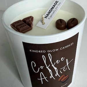 May include: White candle in a white container with the text "Coffee Addict." The candle is decorated with chocolate pieces and coffee bean shapes. A tag reads "HANDMADE Especially for You."