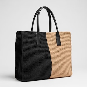 May include: A two-tone tote bag with a black and tan woven design. The bag features black leather handles and accents. The tote bag is rectangular and has a spacious interior, suitable for carrying various items.