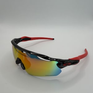 May include: Sport sunglasses with a black frame and red arms. The lenses have a gradient of colors, including yellow, orange, and blue. The brand name is visible on the lens.