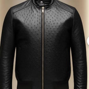 Può includere: Giacca bomber in pelle nera con motivo strutturato. La giacca presenta un collo alto, una cerniera a tutta lunghezza e polsini e orlo a coste. La giacca è esposta su un manichino.