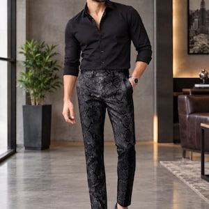 Könnte beinhalten: Ein langärmeliges, schwarzes Hemd mit Knopfleiste kombiniert mit einer dunkelgrauen Hose mit Schlangenledermuster. Das Outfit umfasst schwarze Leder-Loafer mit Metalldetail, eine silberne Armbanduhr und eine dunkel getönte Sonnenbrille.