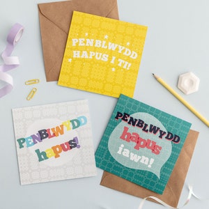 Puede incluir: Tres tarjetas de felicitación coloridas con fondo blanco y diseño estampado. Las tarjetas presentan la frase galesa "Penblwydd Hapus" que se traduce como "Feliz cumpleaños".