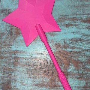 May include: A vibrant pink star-shaped wand with a textured handle. The wand is made of plastic and has a solid, bright colour. The star has five points and a flat surface. The handle is long and cylindrical.