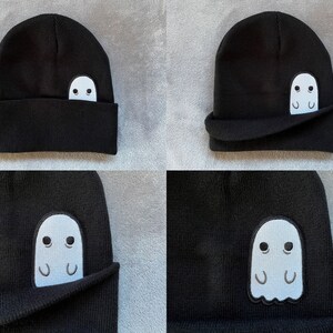 Pu&ograve; includere: Berretto nero con un fantasma bianco ricamato sul lato. Il fantasma spunta da sotto il bordo piegato del berretto.