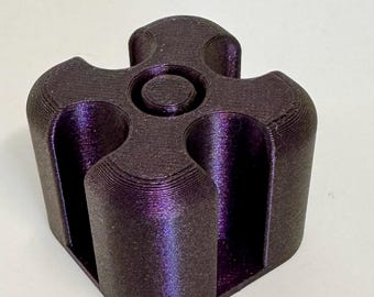 May include: A dark purple, 3D-printed object with a unique, geometric design. The object has a cylindrical base with four curved, vertical slots and a central circular indentation on top. The surface has a textured appearance.