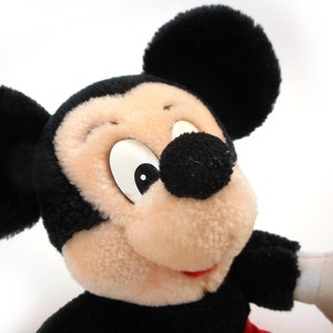 K&ouml;nnte beinhalten: Ein Pl&uuml;schtier Mickey Mouse in Schwarz und Wei&szlig; mit gro&szlig;en Ohren und einem breiten L&auml;cheln. Das Spielzeug ist aus weichem, flauschigem Stoff und hat ein klassisches Mickey Mouse-Design.