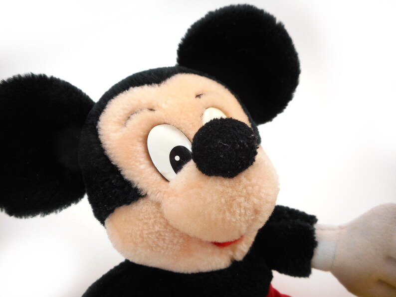 K&ouml;nnte beinhalten: Ein Pl&uuml;schtier Mickey Mouse in Schwarz und Wei&szlig; mit gro&szlig;en Ohren und einem breiten L&auml;cheln. Das Spielzeug ist aus weichem, flauschigem Stoff und hat ein klassisches Mickey Mouse-Design.
