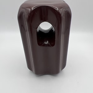 May include: A dark brown, glossy cabinet knob. The knob has a rectangular shape with a rounded top and a central hole. The sides are slightly curved, and the overall design is simple yet elegant.