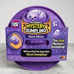 Puede incluir: Un empaque circular morado para el juguete The Original Mystery Dumpling Ghost Edition. El frente presenta un gráfico de un personaje de bola de masa morada con un fantasma, el texto "Crazy Fun", "Ages 3+" y "Will You Find The Super Rare Ghost Dumpling?"