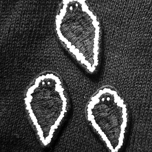 May include: Close-up of a black knit fabric with three white-outlined ghost appliqués. Each ghost has two small white dots for eyes. The fabric has a textured appearance.