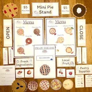 May include: A collection of miniature pie stand accessories, including menus, signs, and pie replicas. The menu displays various pie flavors like pumpkin, chocolate, and cherry. Signs read "Mini Pie Stand," "Open," and "Close." The set includes pie slices and ingredient labels.