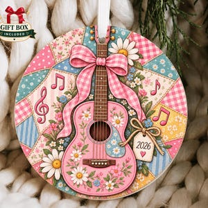May include: A round ceramic ornament featuring a pink acoustic guitar decorated with white daisies and green leaves. The background is a patchwork of pink, blue, and yellow floral and gingham patterns with musical notes and a tag labelled 2026.