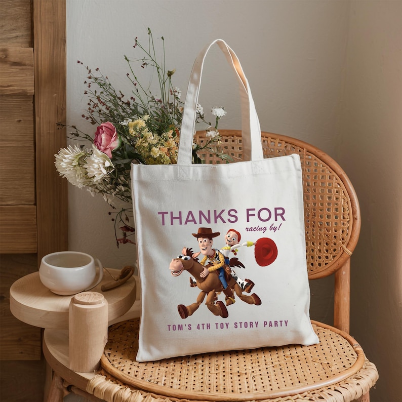 May include: A white canvas tote bag featuring a graphic of Woody and Jessie from Toy Story riding Bullseye. The text reads "THANKS FOR racing by!" and "TOM'S 4TH TOY STORY PARTY" in purple lettering. The bag has two fabric handles.