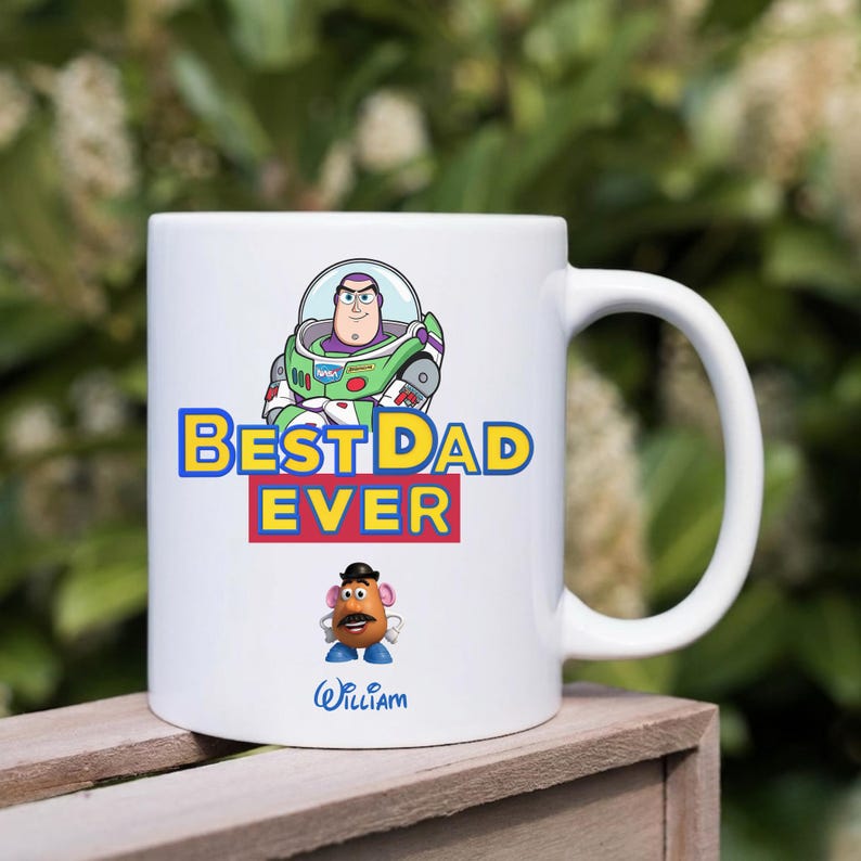 Puede incluir: Una taza de cer&aacute;mica blanca con un gr&aacute;fico de Buzz Lightyear sobre el texto BEST DAD EVER en amarillo y rojo. Debajo del texto hay un peque&ntilde;o personaje del Se&ntilde;or Patata y el nombre William escrito en azul en la parte inferior de la taza.