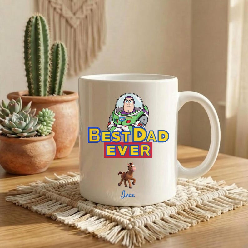 Puede incluir: Una taza de cer&aacute;mica blanca con un gr&aacute;fico de Buzz Lightyear sobre el texto amarillo y rojo "BEST DAD EVER" y un peque&ntilde;o personaje de caballo marr&oacute;n debajo, con el nombre "Jack" escrito en letra cursiva azul en la parte inferior.