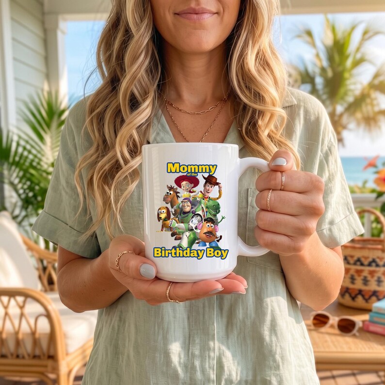 May include: A white ceramic mug featuring a colorful graphic of Toy Story characters including Woody, Buzz Lightyear, Jessie, and Mr. Potato Head. The text "Mommy of the Birthday Boy" is printed in blue and yellow letters above and below the characters.