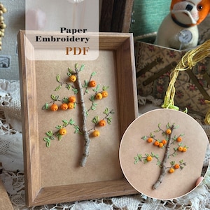 May include: A framed paper embroidery piece showing a tree with orange fruit and green leaves. The frame is wooden. The text "Paper Embroidery PDF" is visible. A second, circular embroidery piece is in the lower right. The measurements are in centimetres.
